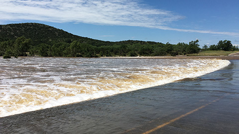 Roadway along the Nueces River with floodwater flowing across the road