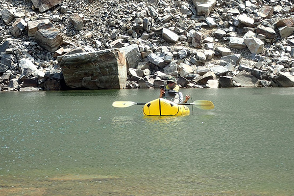 Researcher on a small river, in a bright yellow inflated raft, has lowered a sensor into the water and is reading results from a handheld device.