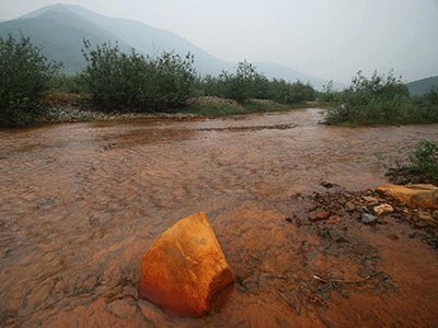 Bright orange rock in the middle of a waterway with clearly orange sediments