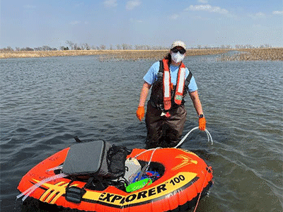Researcher standing in hip-deep water, pulling an orange inflatable holding sampling gear