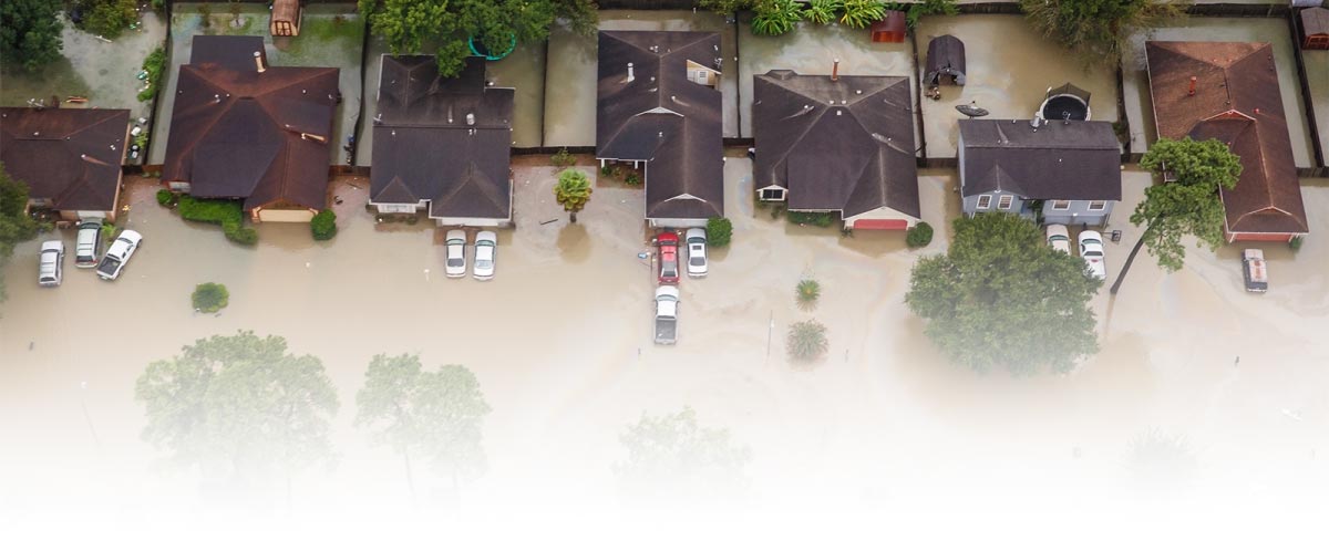 Aerial view of urban flooding with homes and vehicles submerged in standing water.