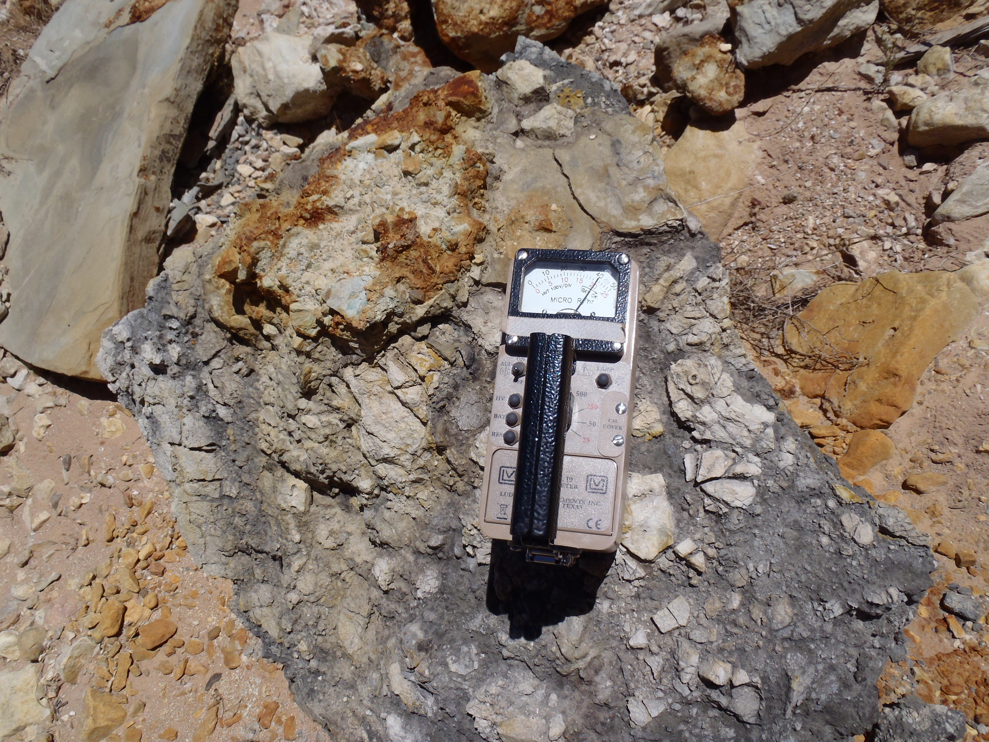  View of gray/black boulder containing multiple smaller boulders with a Ludlum Model 19, Micro R reader registering a reading of 500 micro R per hour on the 0-500 scale of the meter. 