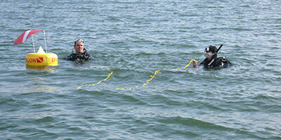 Two scuba divers in the water near a safety buoy